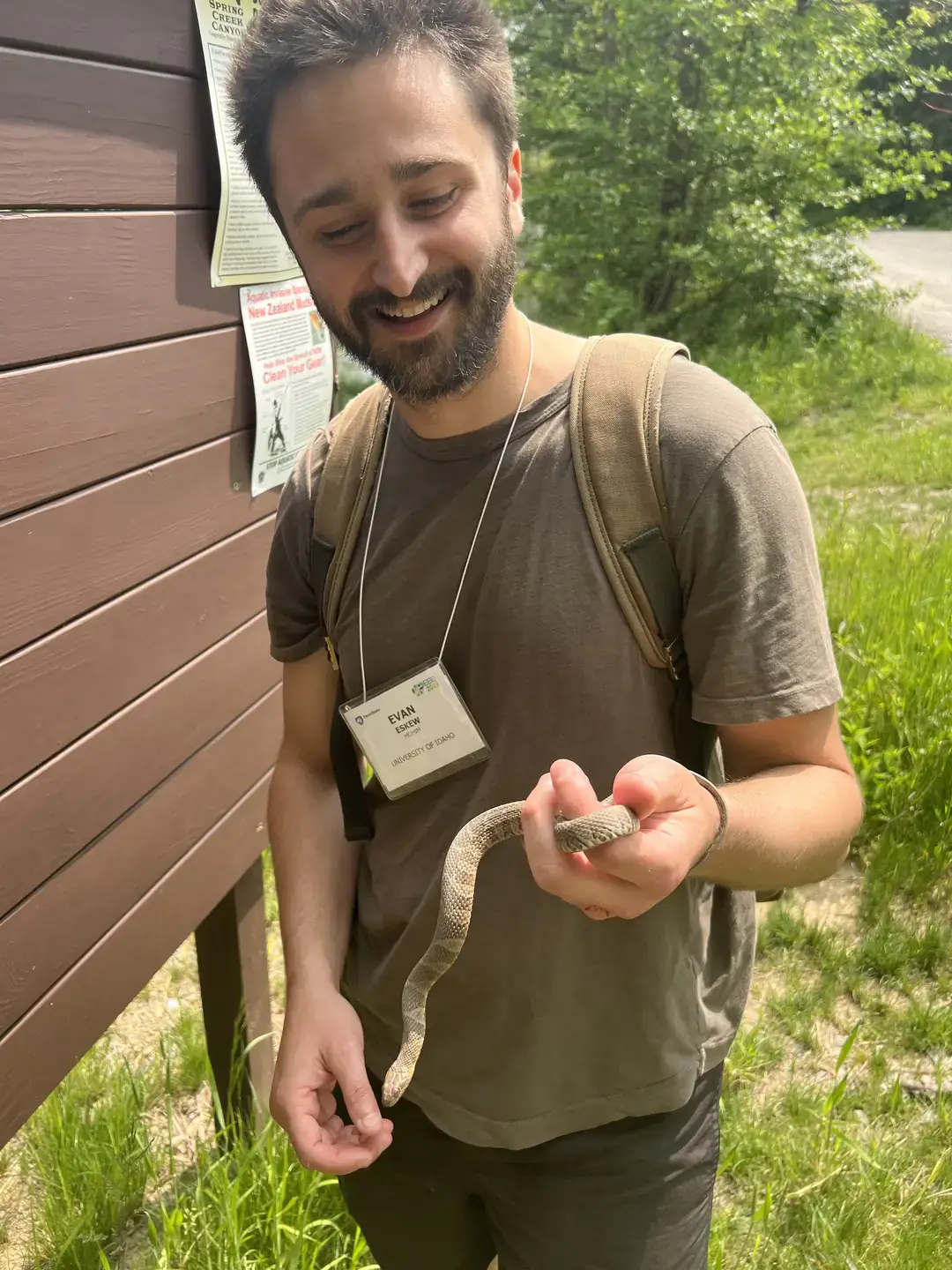 Bearded man in T-shirt smiles while handling a snake.