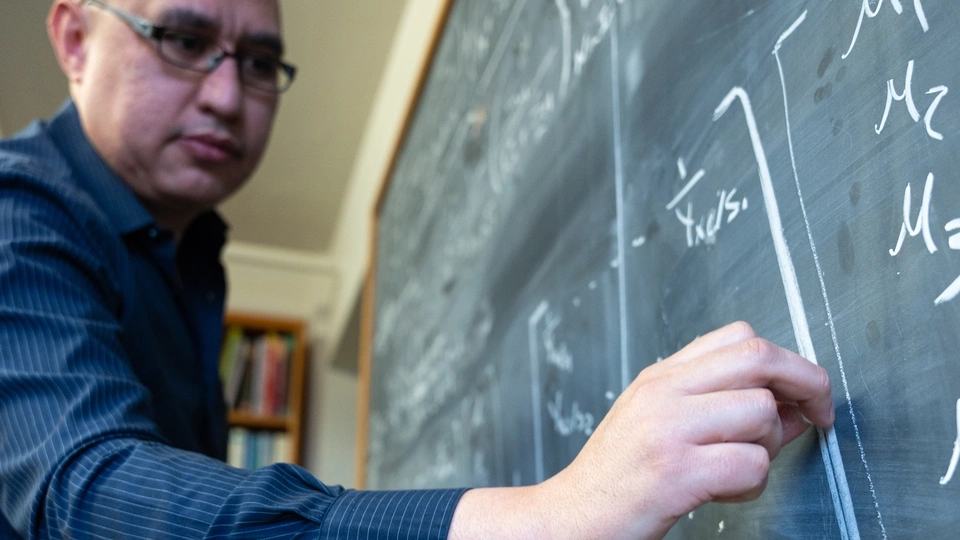 Assistant Professor of Mathematics, Esteban Hernandez-Vargasriting, presenting math equations model on a chalkboard to study the mitigation of viral infections.