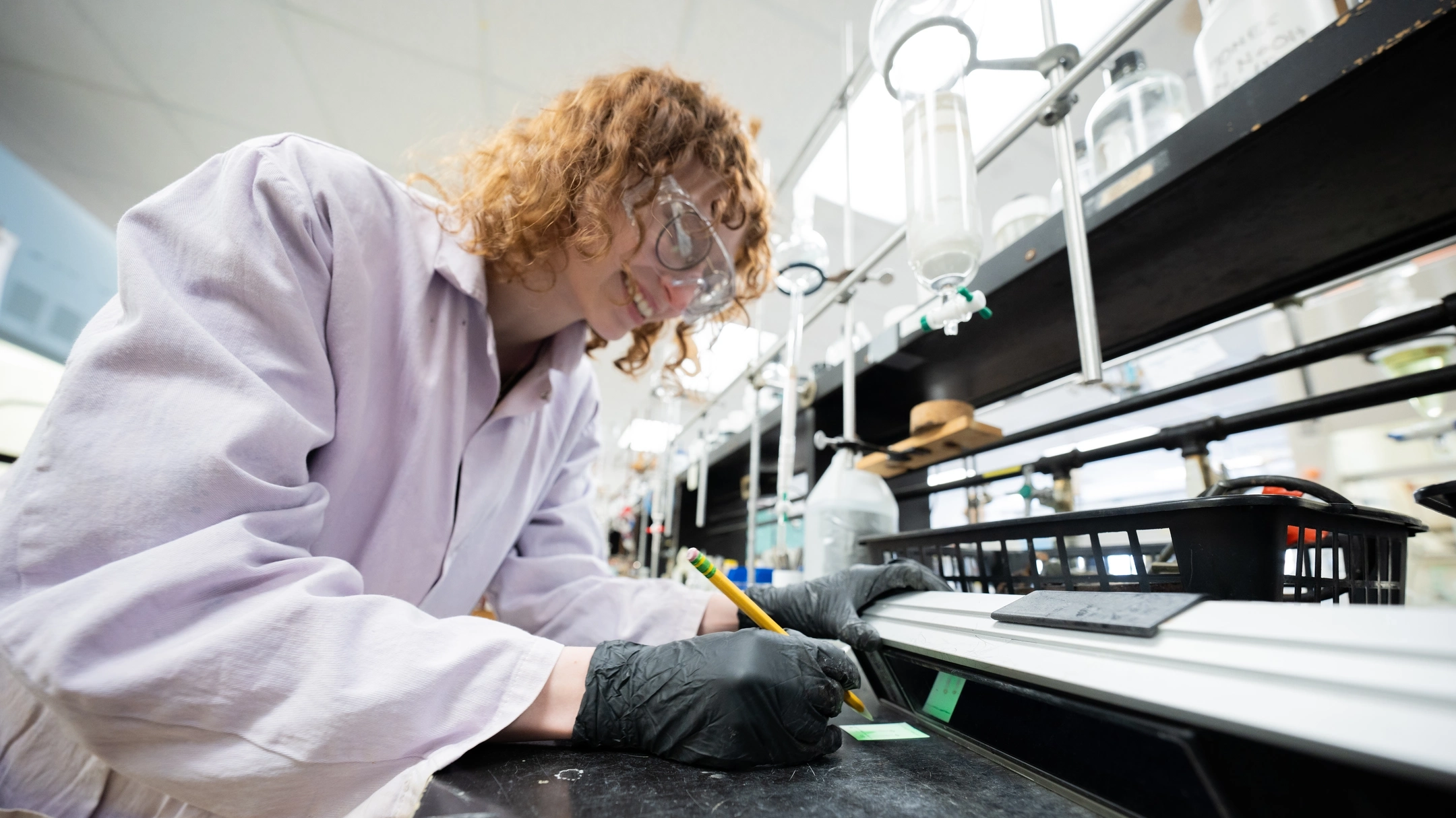Student in a lab coat and goggles writing labels in chemistry lab