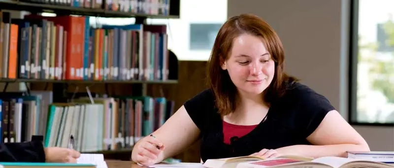 Woman in library at desk looking at book