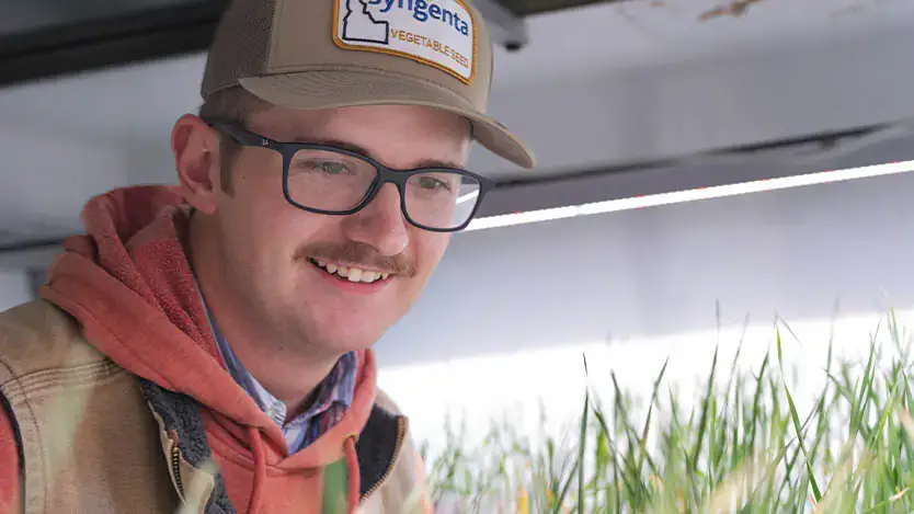 A man smiles while examining crop growth in a greenhouse.