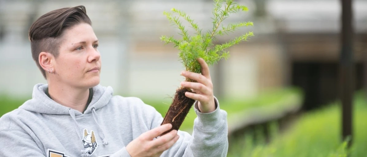 student wearing vandal sweater holding tree in early stages of growth