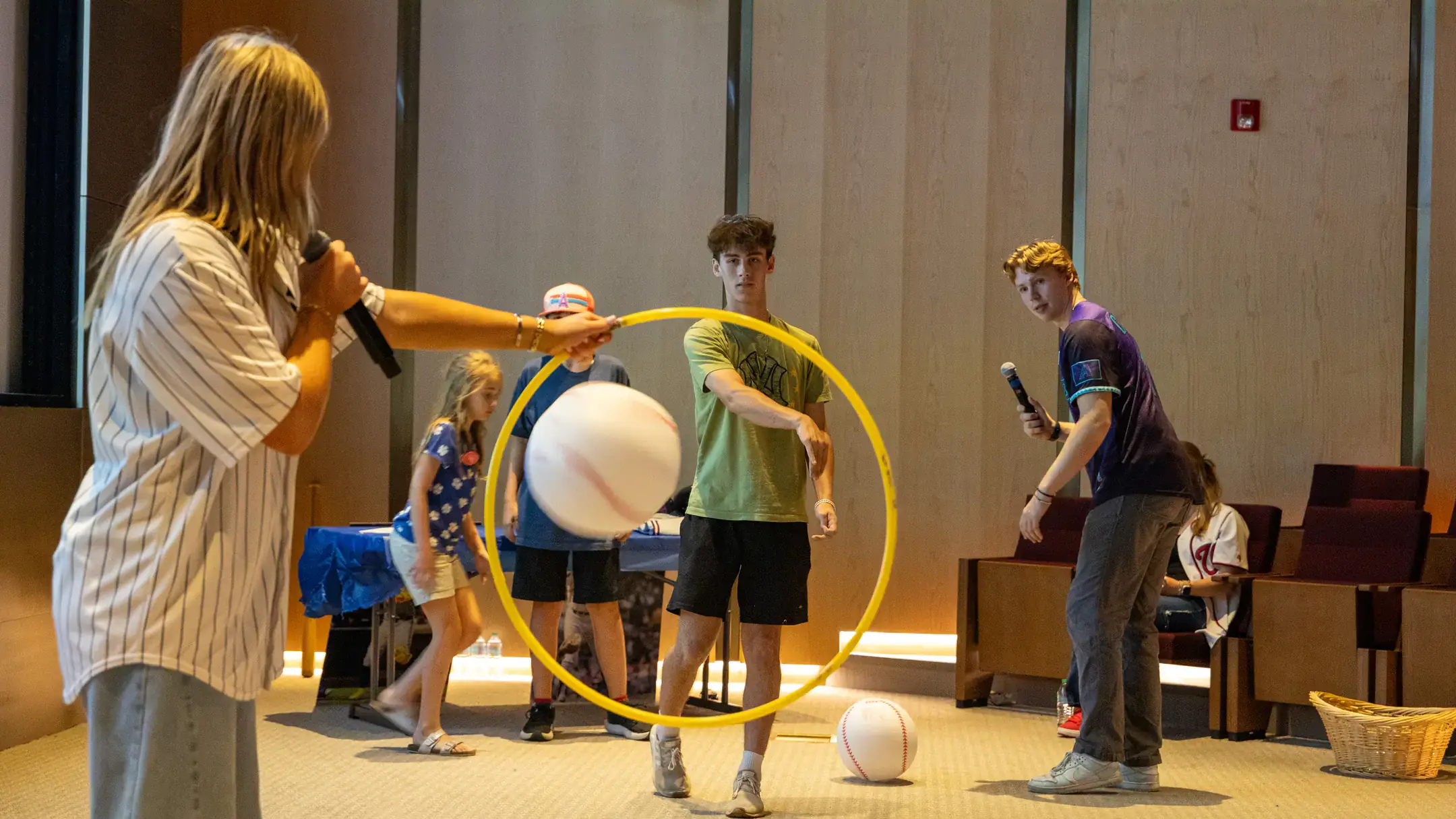 Woman holding a yellow hoop and man throwing a ball through the hoop.