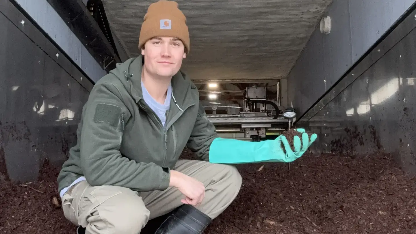  A researcher kneels inside of a composting system housed inside of a storage container, allowing finished compost to run through his fingers.