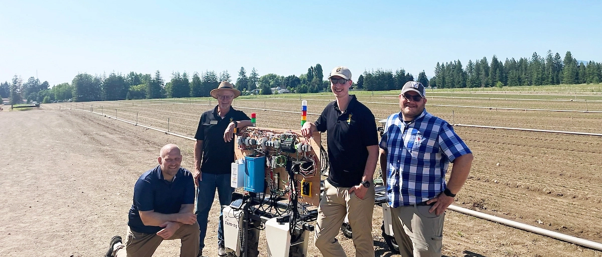U of I students in a field of crops with a robot used to burn weeds.  