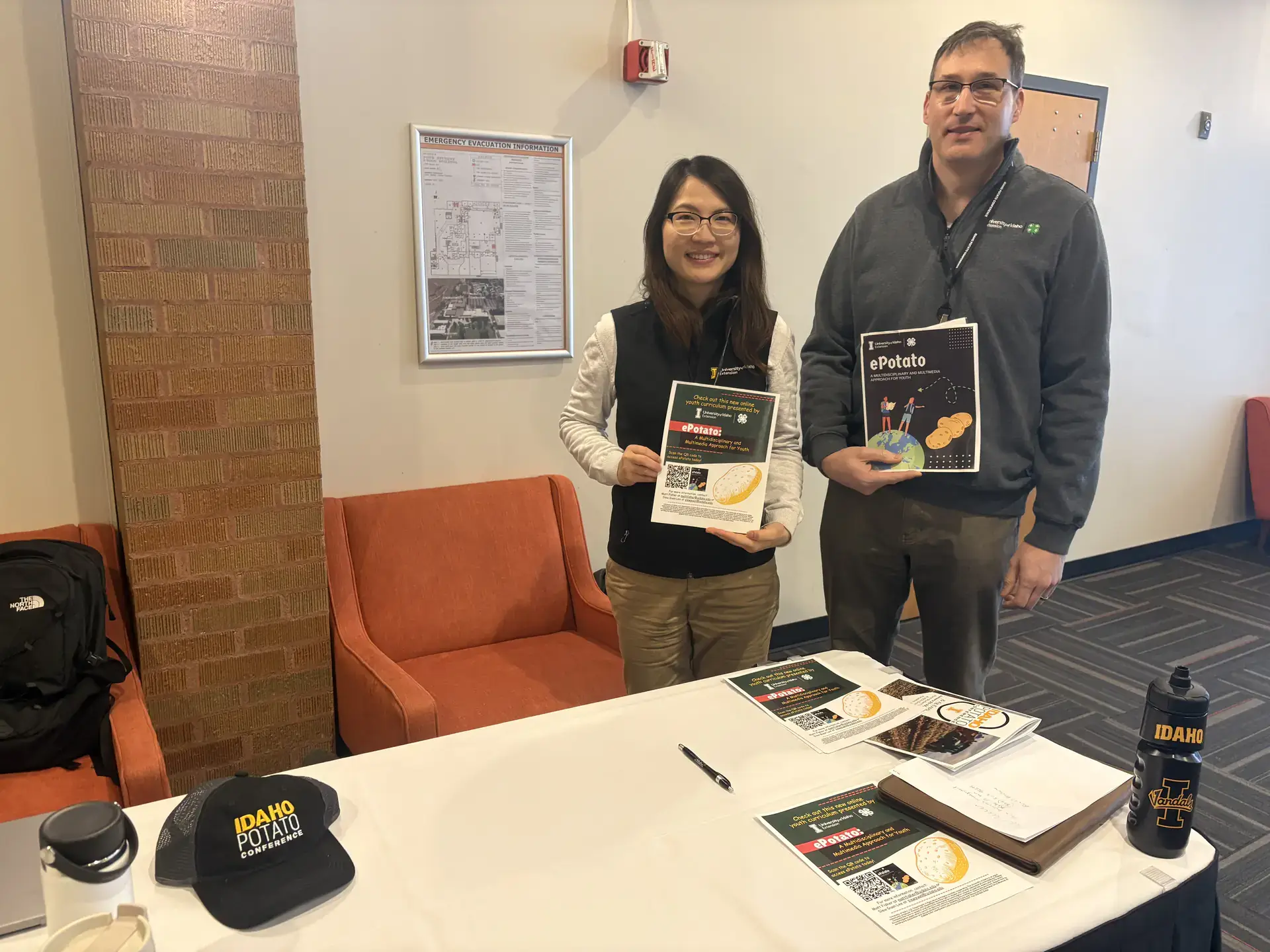 A woman and a man stand by a table holding up flyers with images of potatoes.