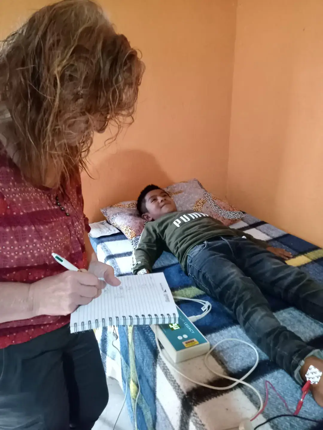 Ginny Lane, CALS assistant professor, writes in a notebook, while a boy in Guatemala lies on a bed nearby.