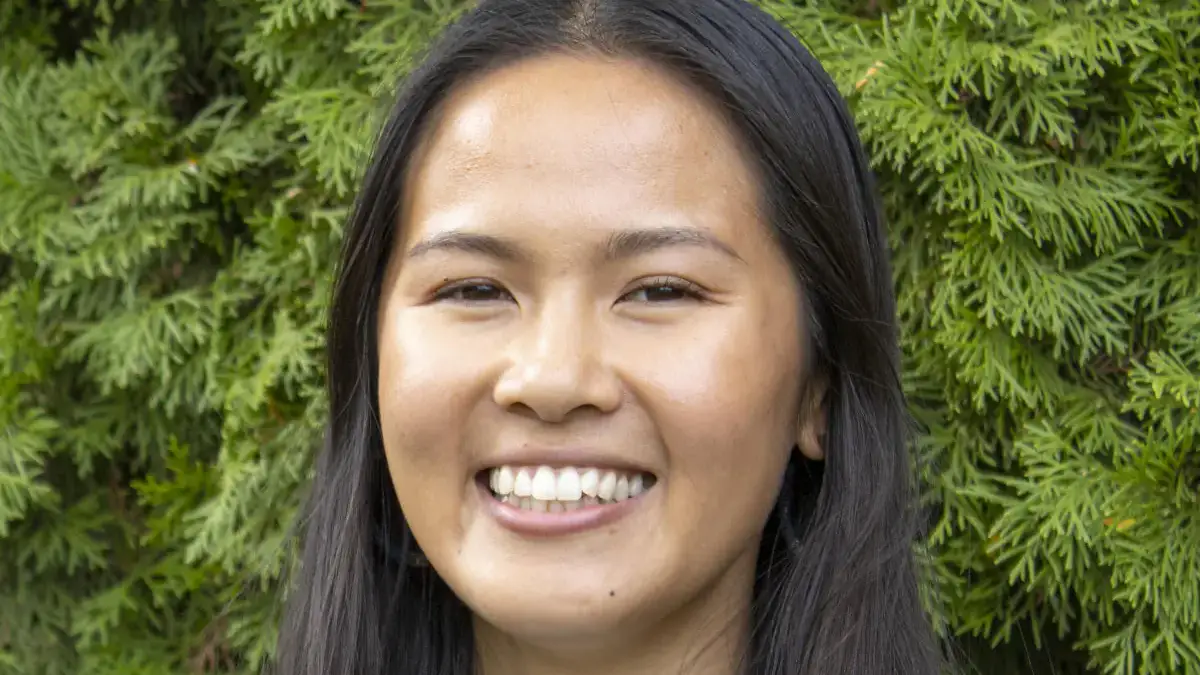A woman with dark brown hair in a sweater smiling at the camera