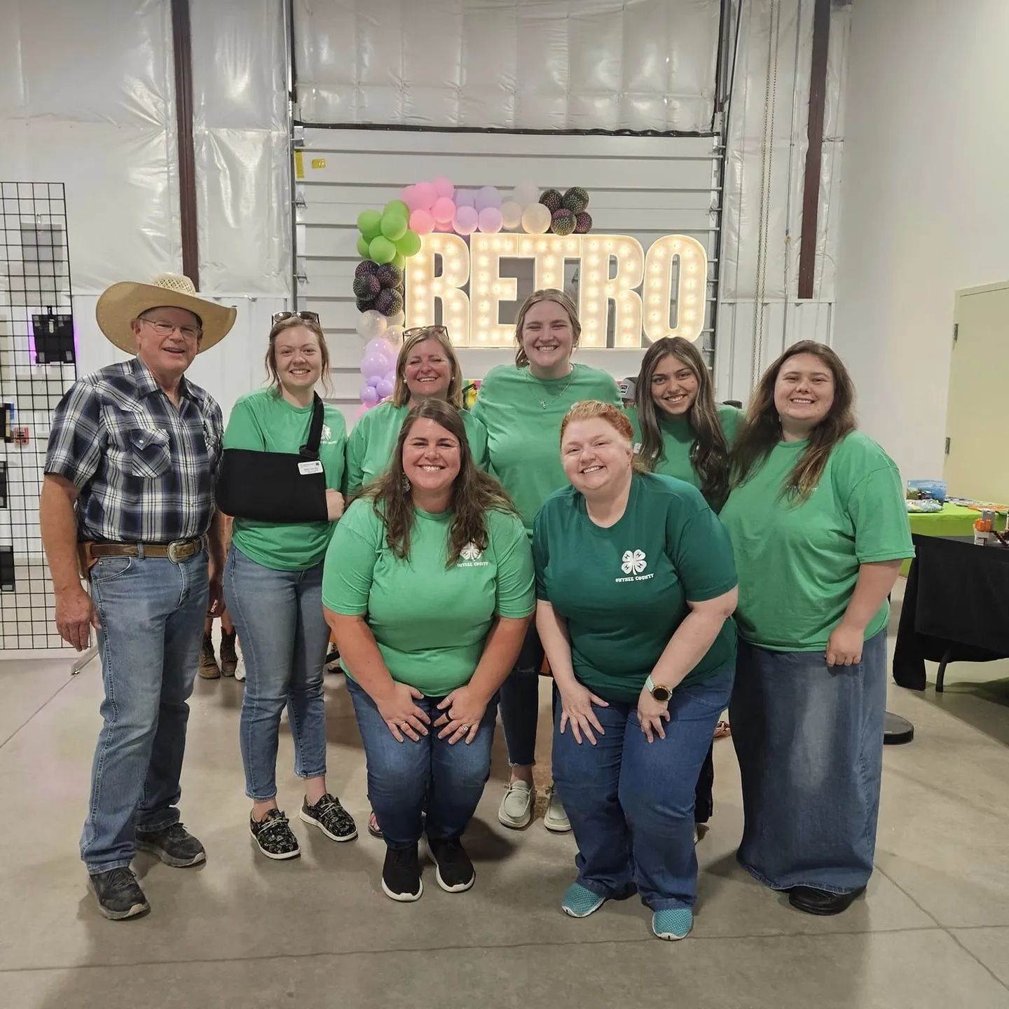 Group in green shirts pose in front of "retro" sign.