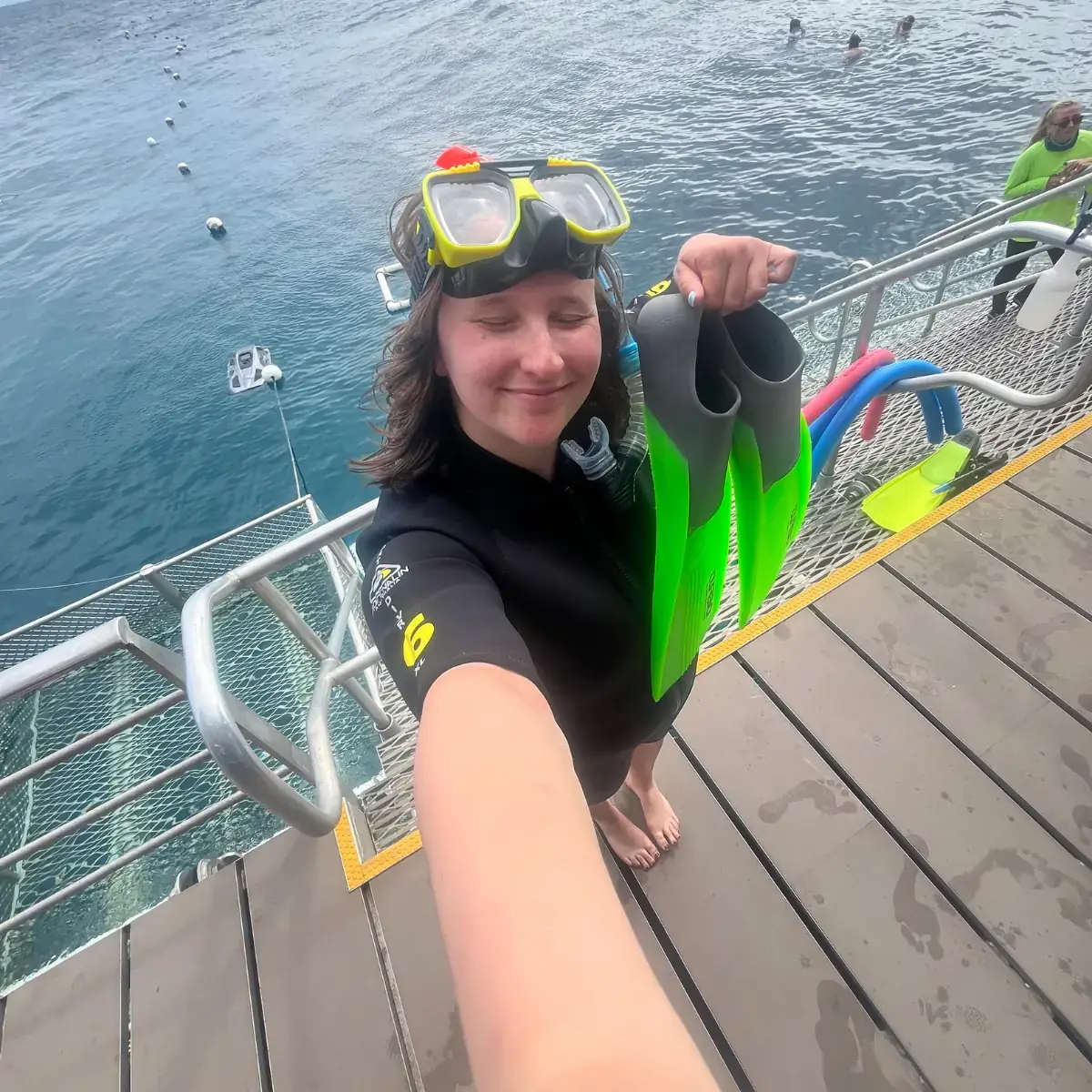 A woman holding flippers in front of water.