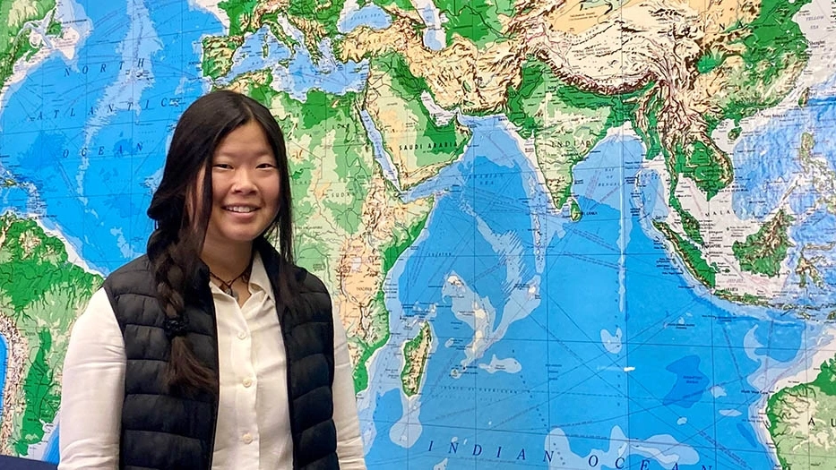 Ruby Crooks smiles in front of a floor-to-ceiling world map.