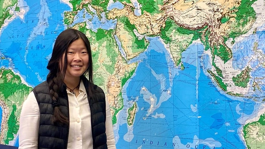 Ruby Crooks smiles in front of a floor-to-ceiling world map.
