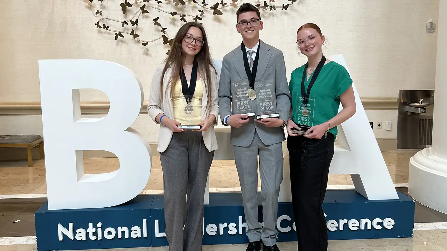 U of I BPA chapter members Rylee Wimer, Colton Moore and Sophia Gill stand in front of a BPA sign and hold their awards. 
