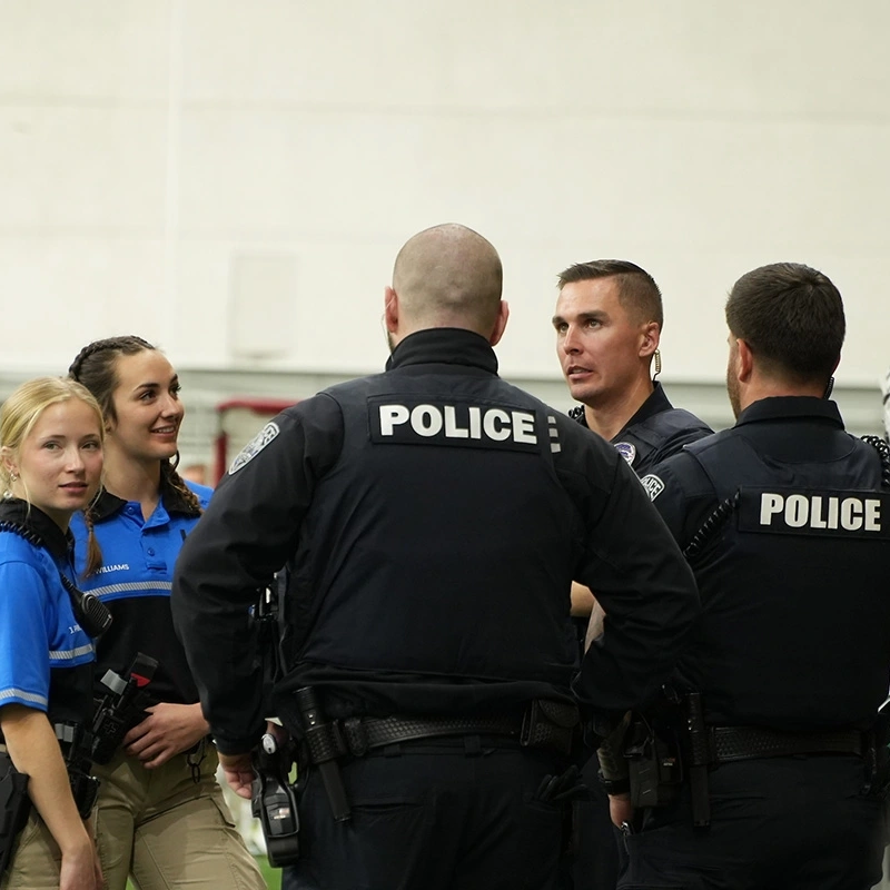 A group of police and volunteers huddle next student football athletes
