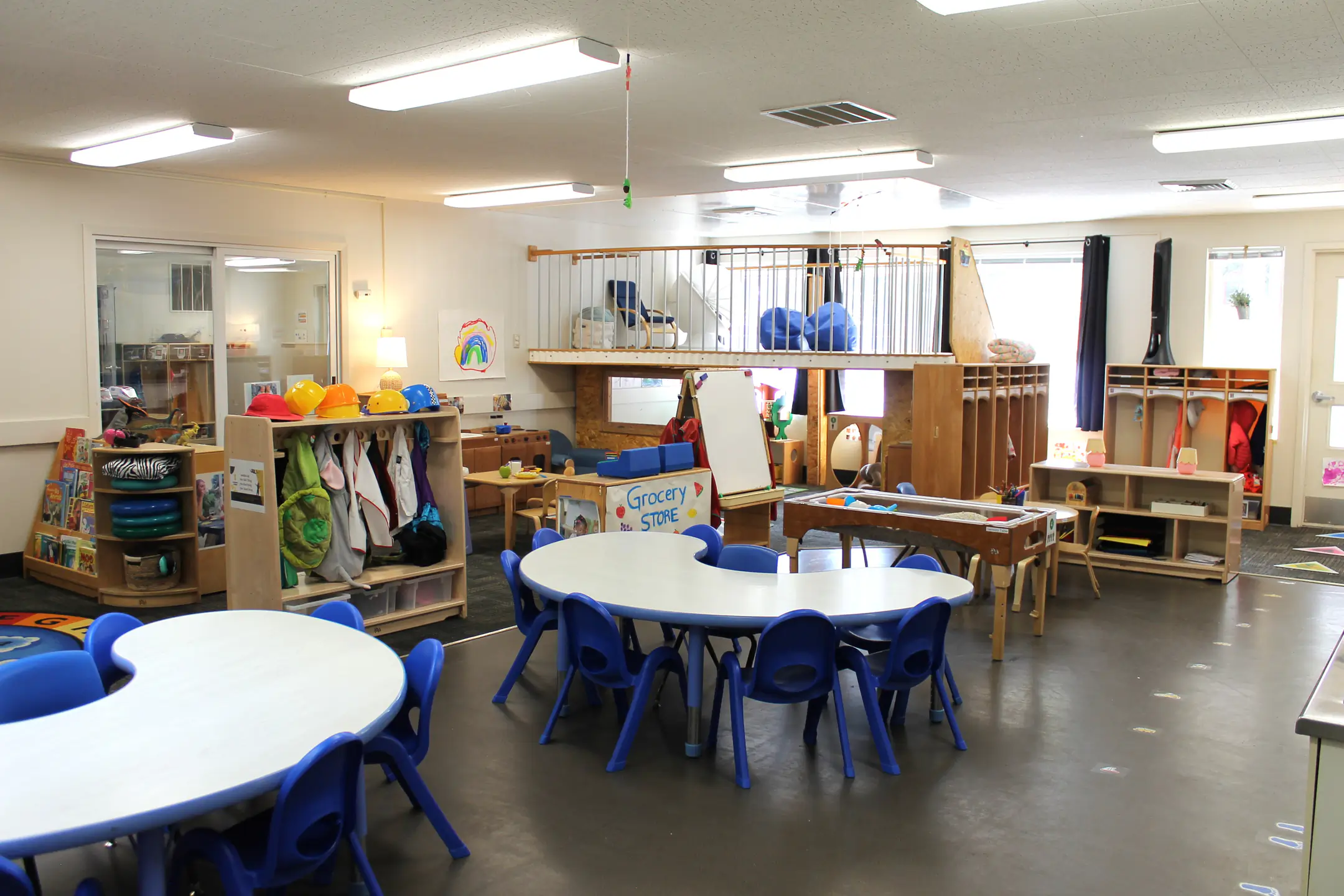 A large classroom with group tables, cubbies, play area, and jungle gym.