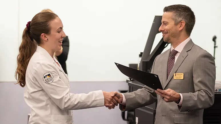 Student shakes hands while presented with an award.