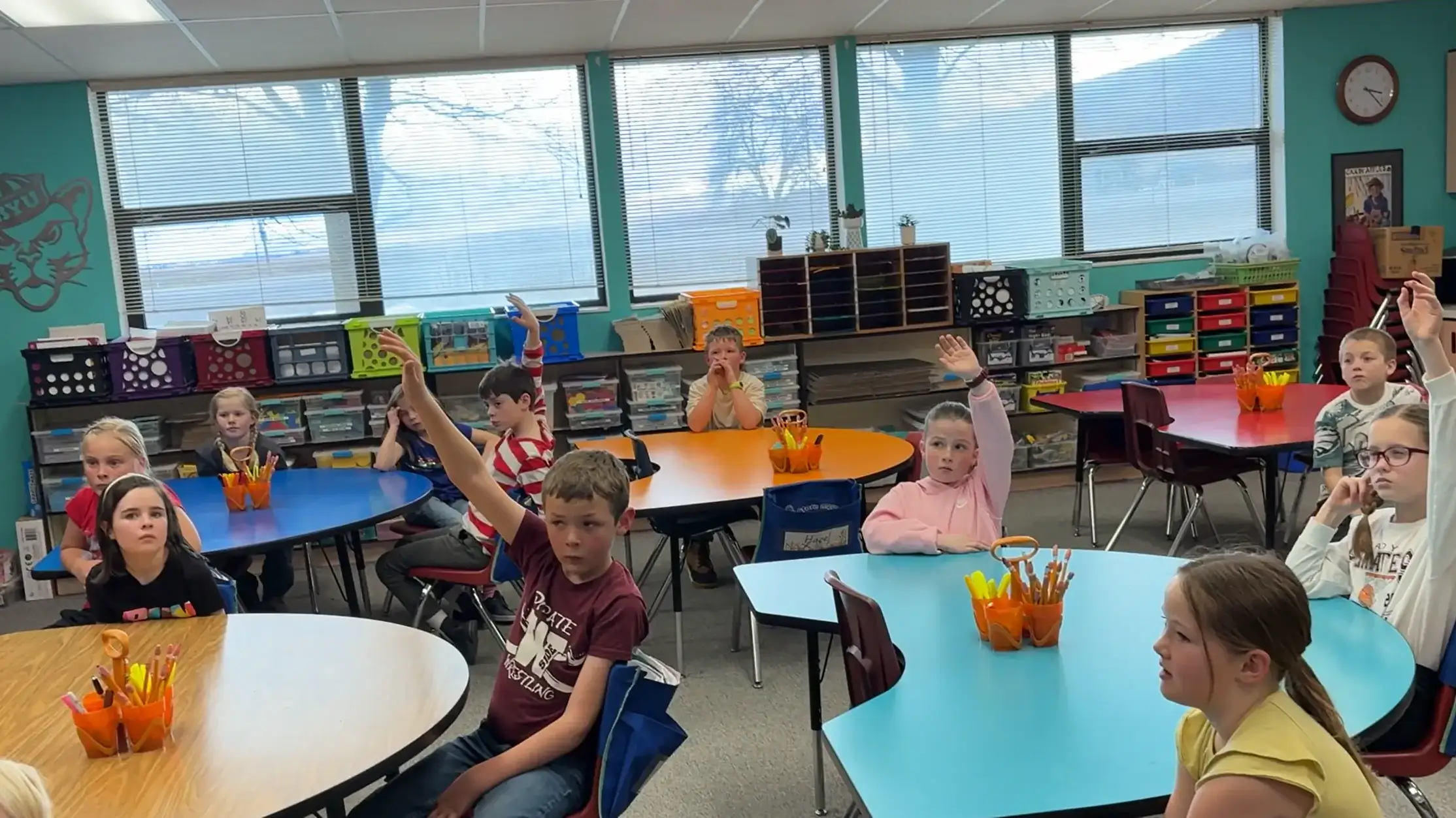 A classroom of children raising their hands to answer a question.