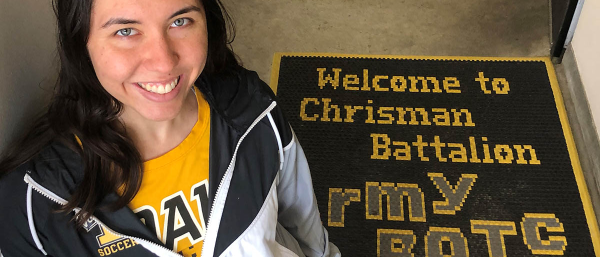 Smiling woman looks up from stairwell with ROTC regalia in background.
