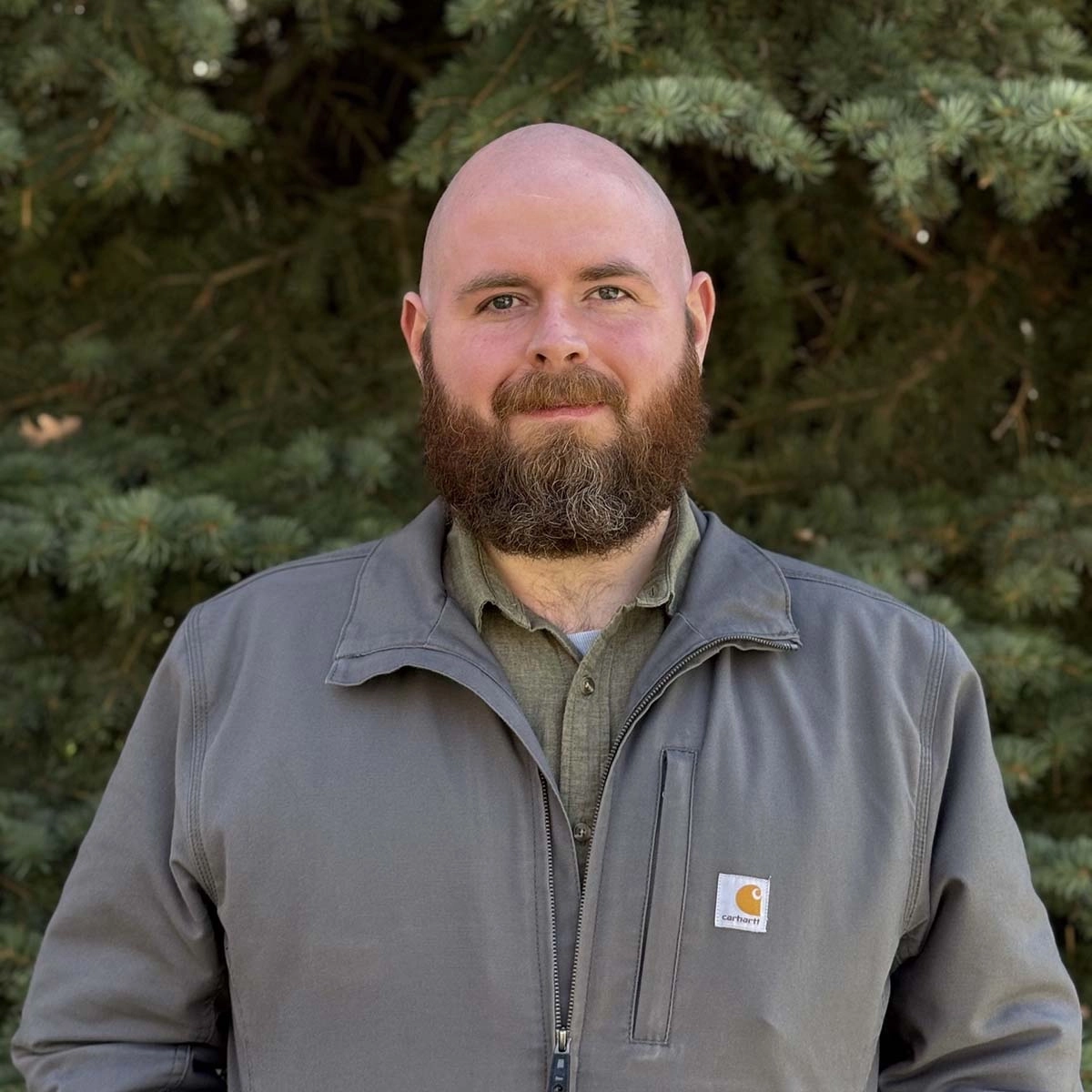 A portrait of a man smiling in front of trees.