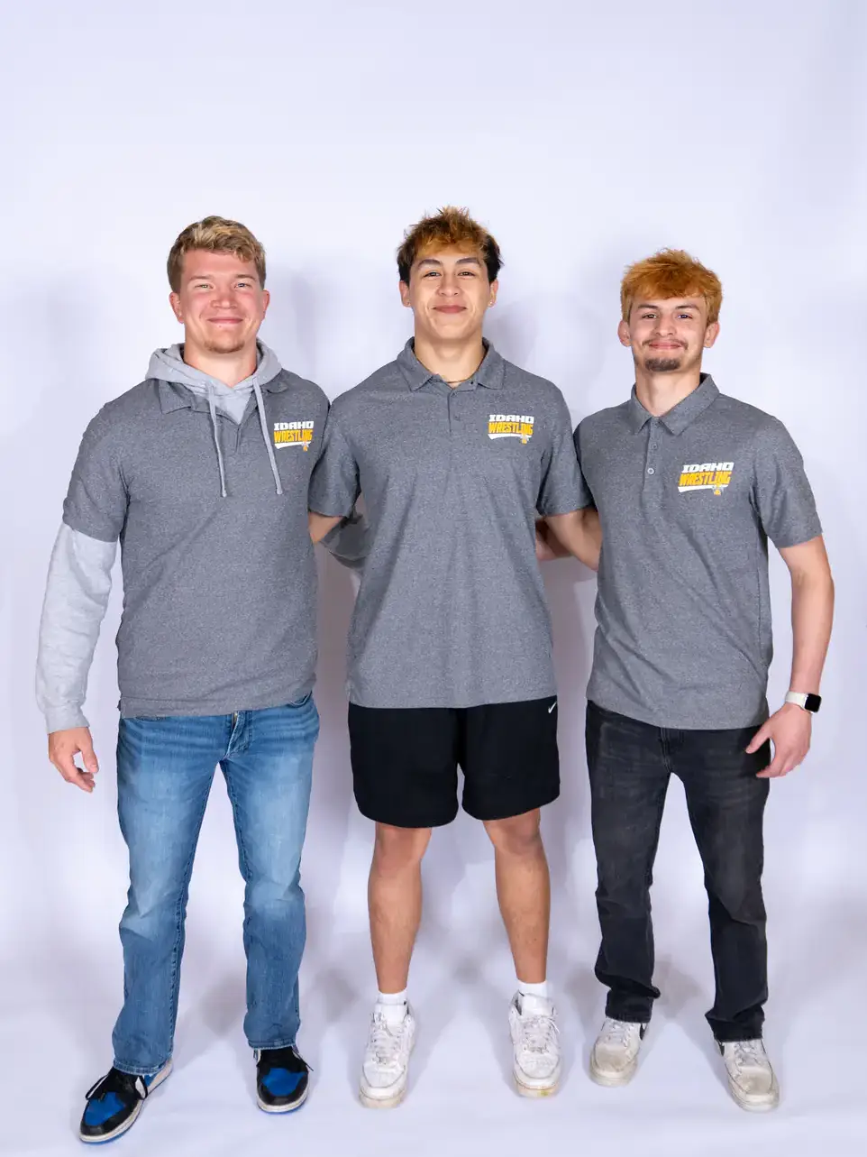 Three men posing in front of white background wearing gray Idaho Wrestling shirts. 